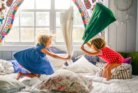 Two young children playing with pillows on a large bed.
