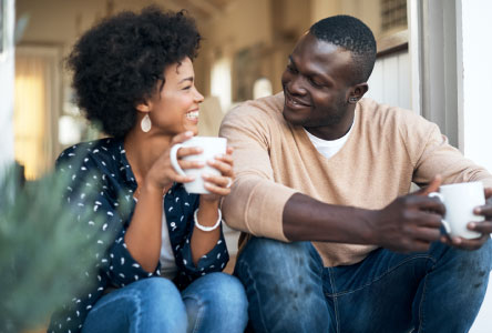 Young couple smiling and sitting together outside while holding coffee mugs.